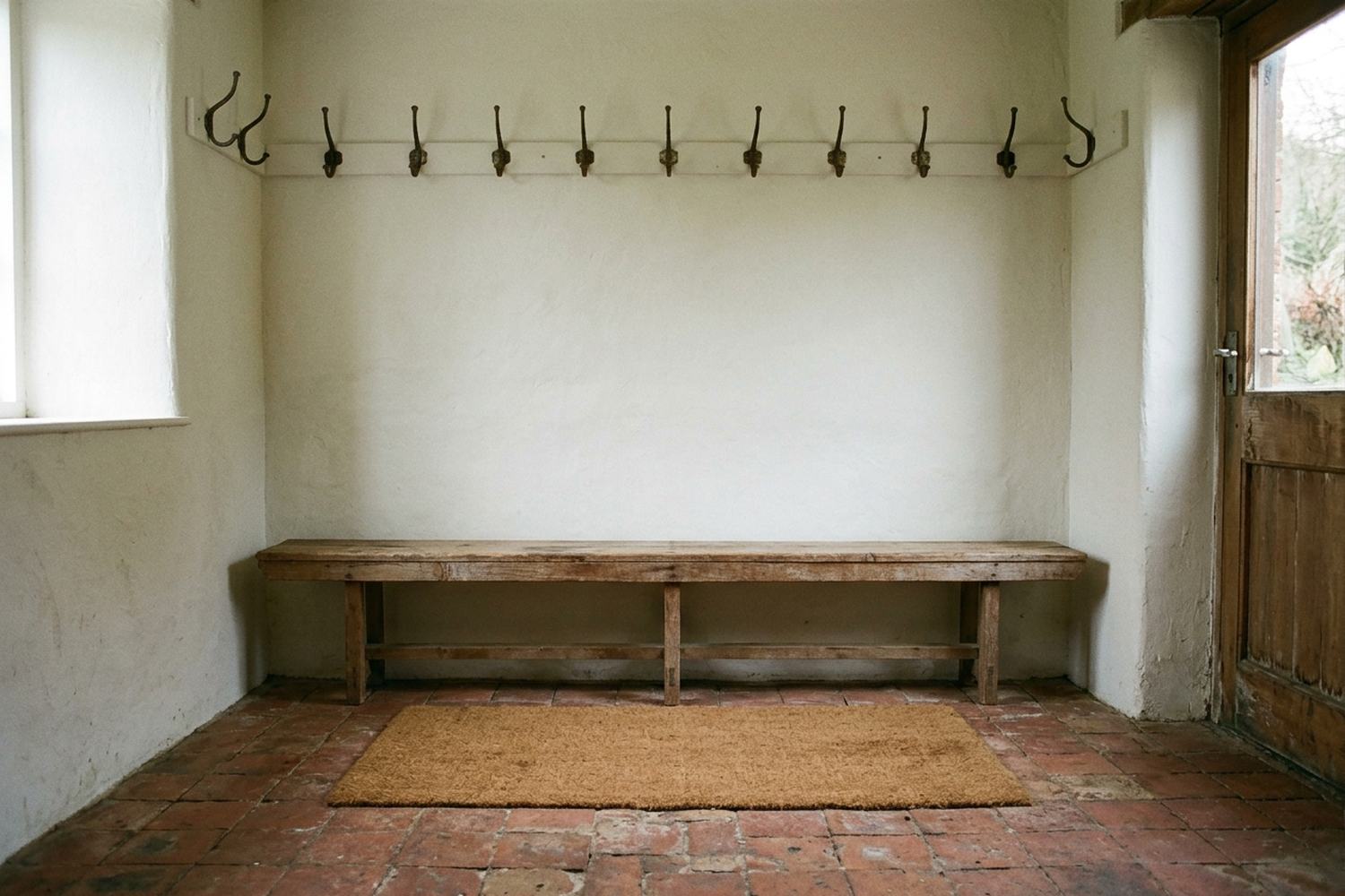 A small tiled boot room with a coir mat, a low bench and empty iron hooks
