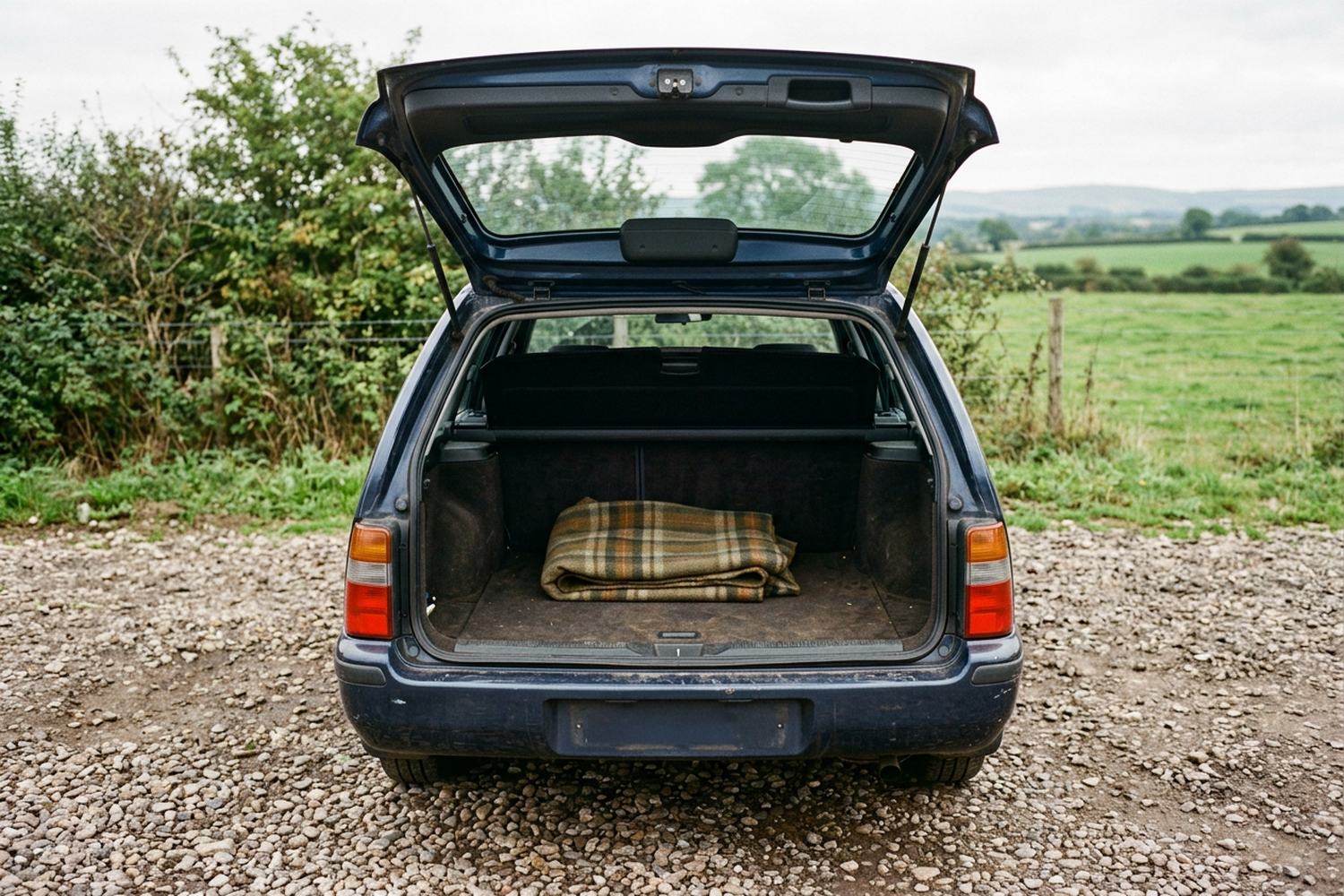 The open tailgate of a plain estate car with a folded wool blanket on it